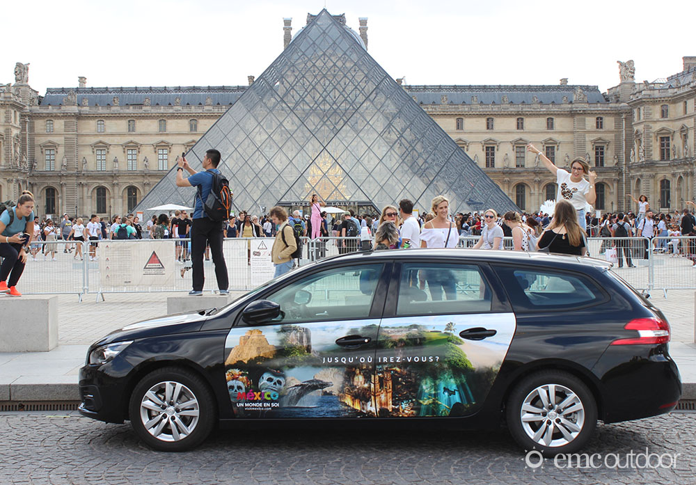 A wrapped vehicle in front of the Louvre displaying advertising for a tourism desitination